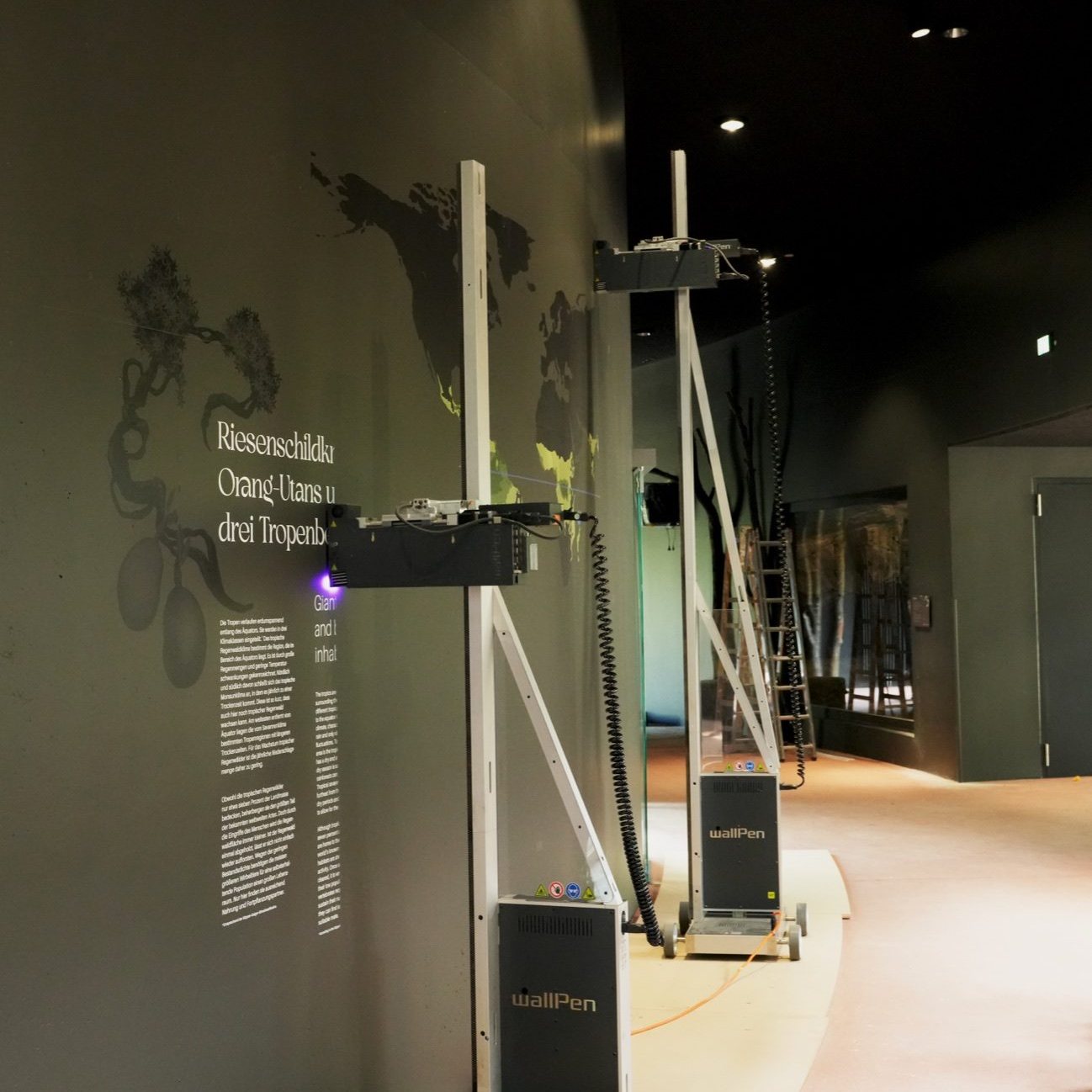 Two direct-to-wall printers printing artwork and text onto an exhibition wall